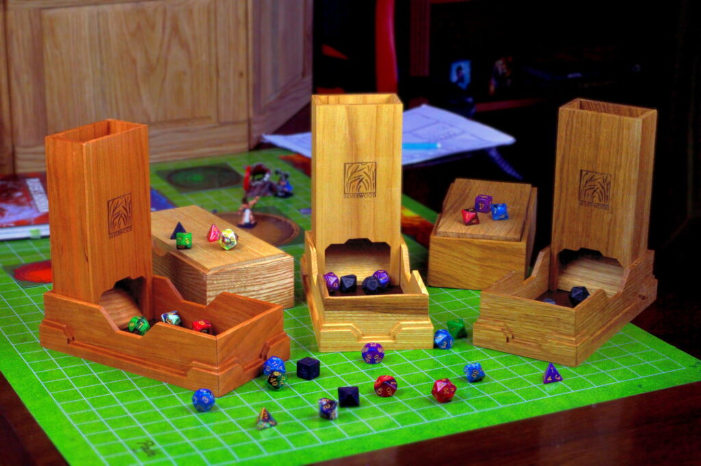 A group of Dice Towers on a gaming table with a mat, lots of dice and a GM screen in the background.